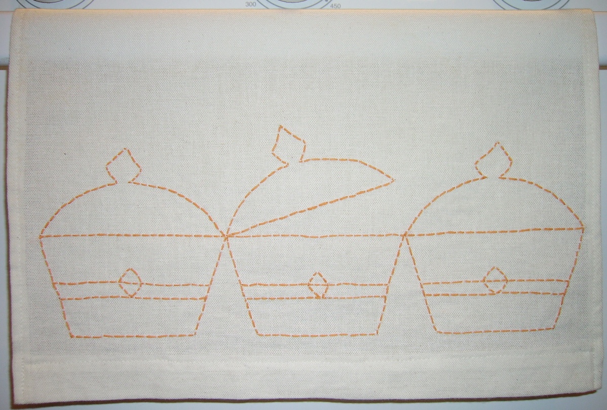Cream linen cloth with hand-stitched orange outline embroidery of basket shapes, laid on a table, crafting mood