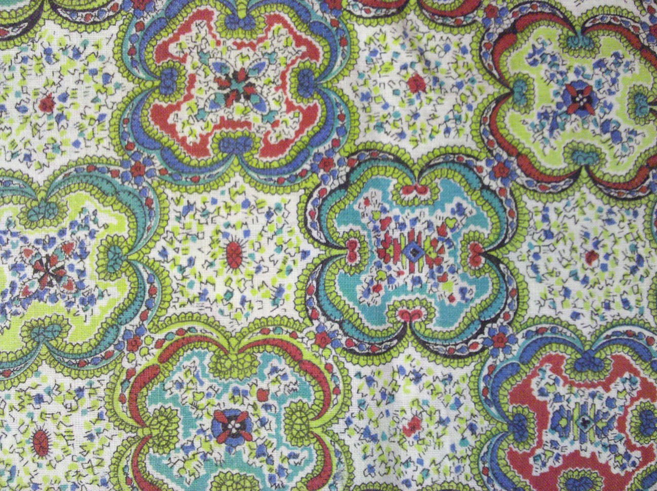 A carved linocut relief print of colorful floral medallion fabric in green, blue, red, and white, decorative textile pattern with rich ornamental detail